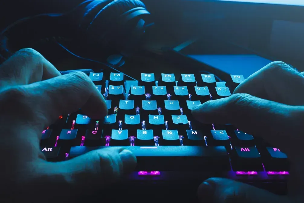Una persona está escribiendo en un teclado con auriculares de fondo.
