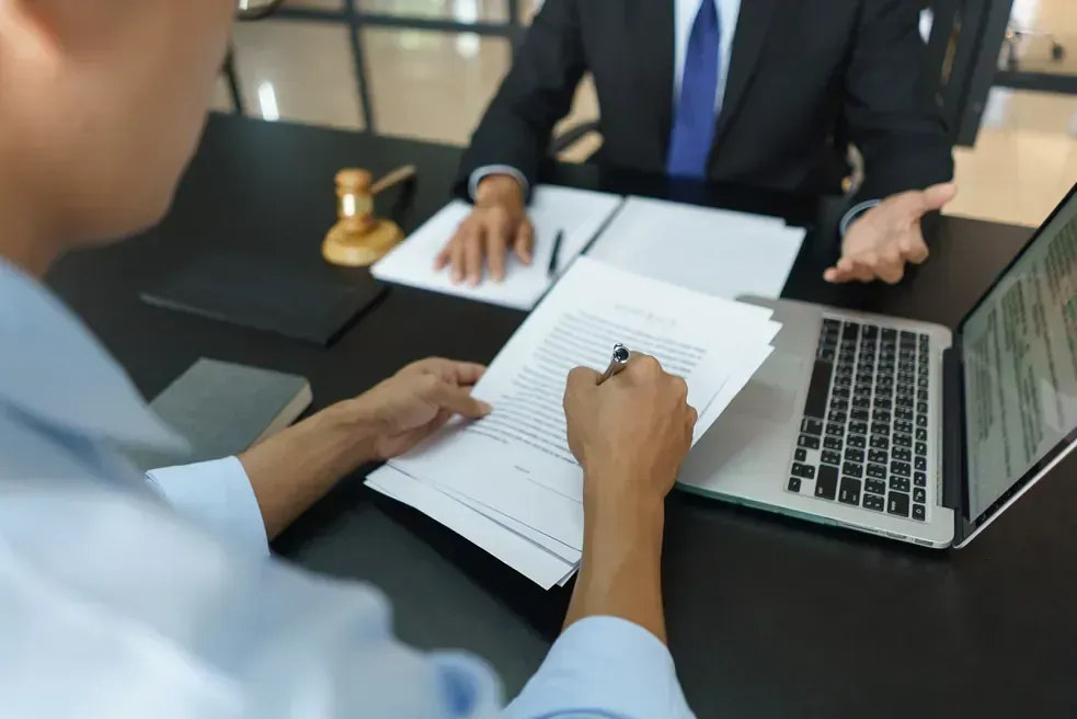 Dos hombres están sentados en una mesa con papeles y una computadora portátil.