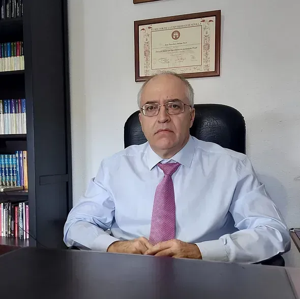 Un hombre con una camisa azul y corbata rosa está sentado en un escritorio.