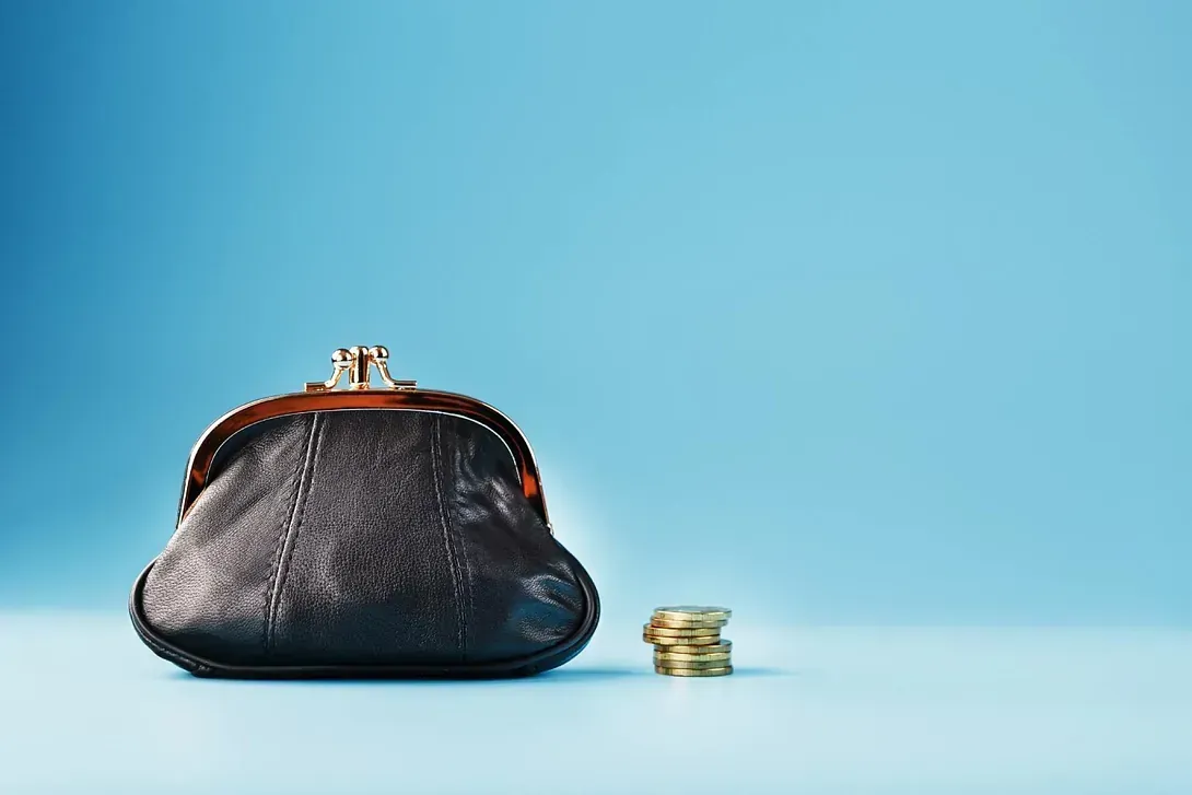 Un bolso vacío y una pila de monedas sobre un fondo azul.