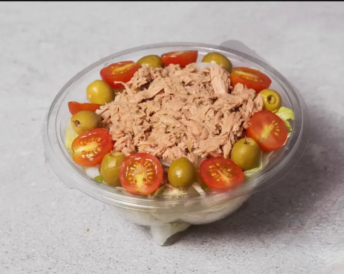 Ensalada de atún en un bol transparente, cubierta con tomates cherry y aceitunas verdes.