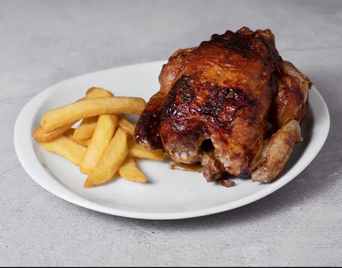 Pollo entero asado en una bandeja para hornear, dorado y glaseado con sus propios jugos.