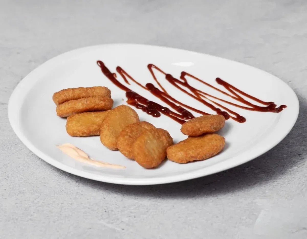 Plato de nuggets de pollo con salsa de tomate rociada sobre un plato blanco.