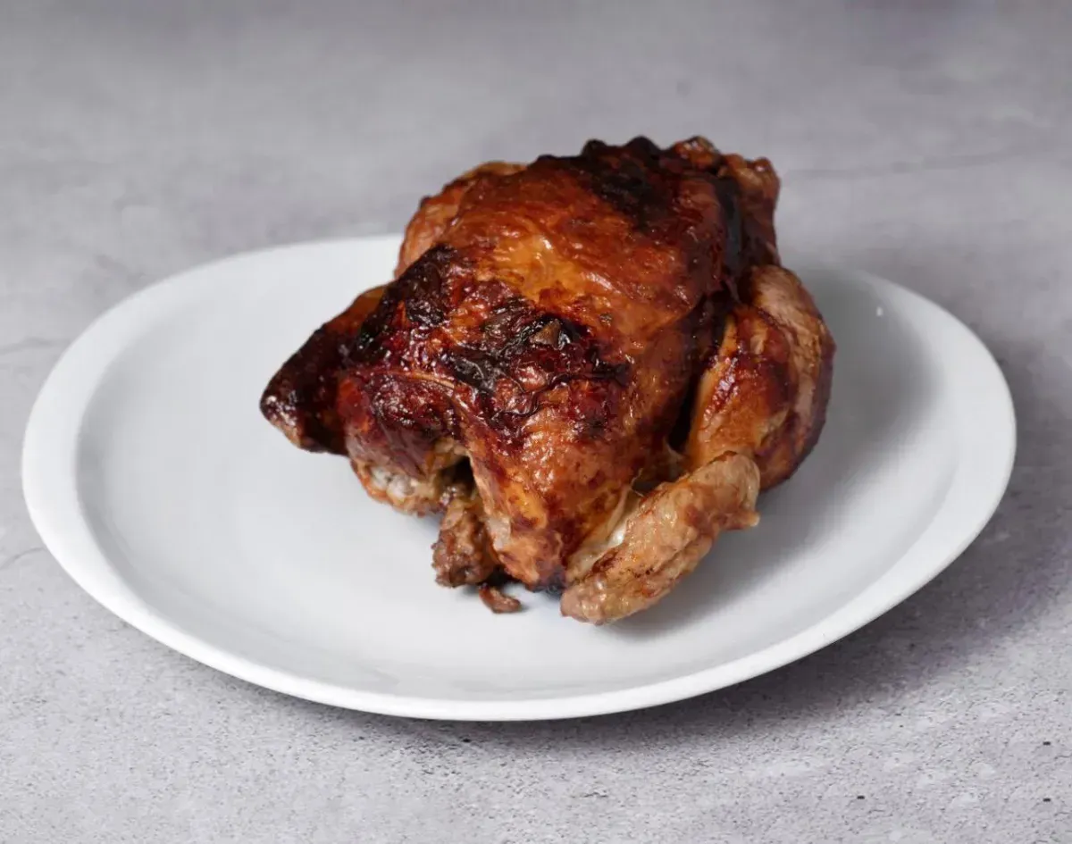 Trozo de pollo asado en un plato blanco sobre un fondo gris.