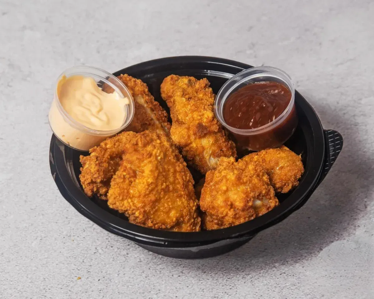 Cesta de pollo frito crujiente con dos salsas para mojar en una bandeja negra.