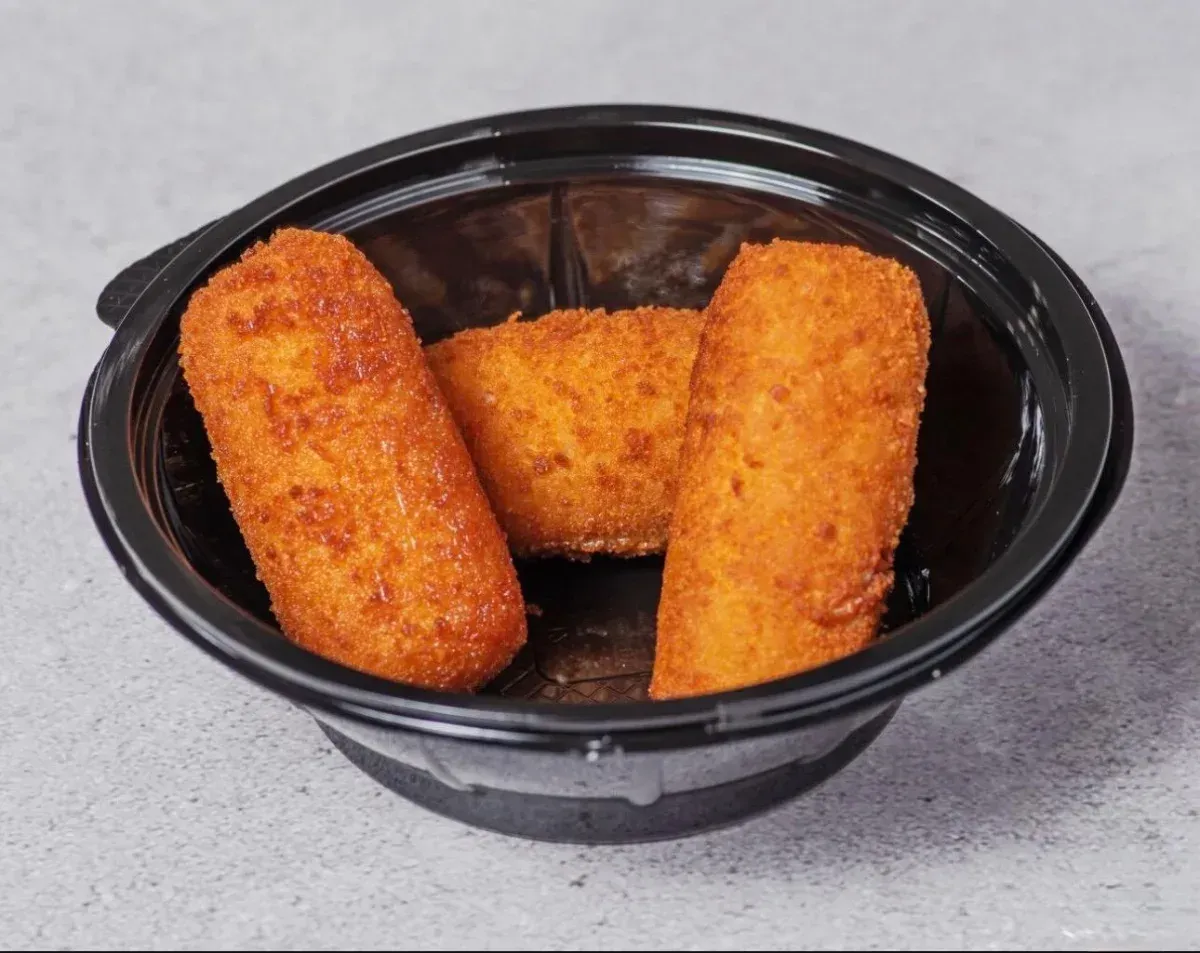 Tres croquetas empanizadas de color marrón dorado en un recipiente de plástico negro.