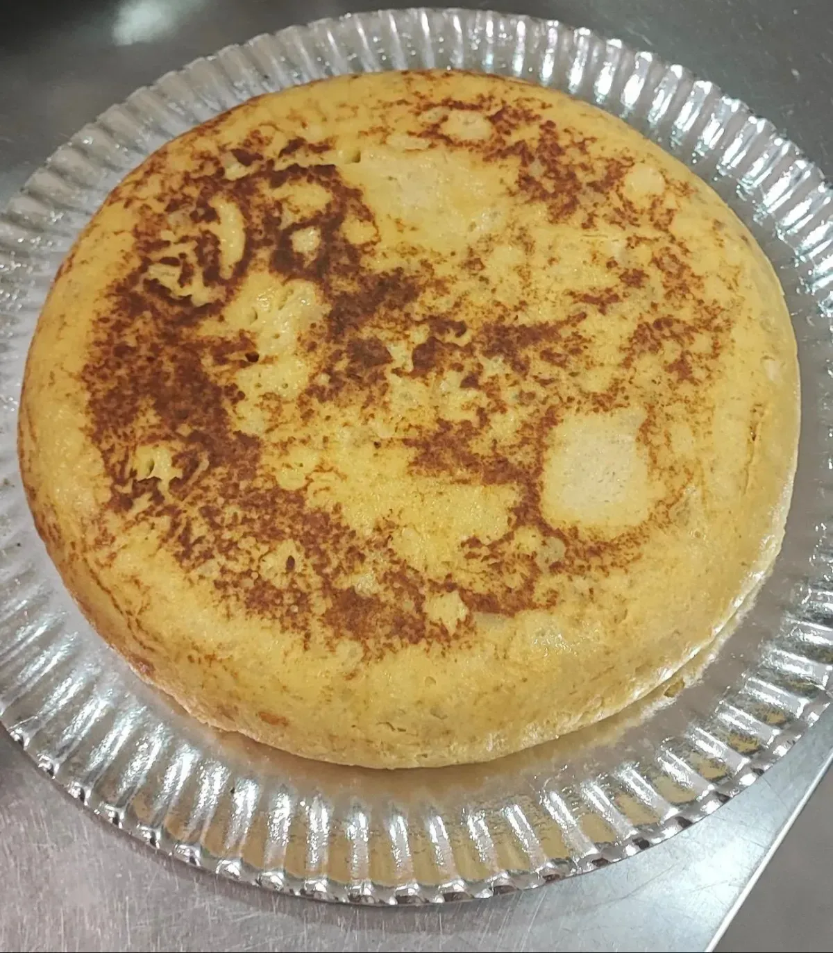 Pastel de color marrón dorado en un molde desechable de aluminio con manchas doradas irregulares en la parte superior.