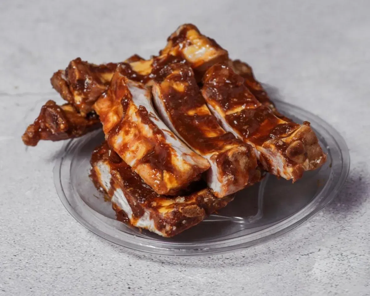 Costillas glaseadas brillantes apiladas en un pequeño plato transparente sobre un fondo gris.