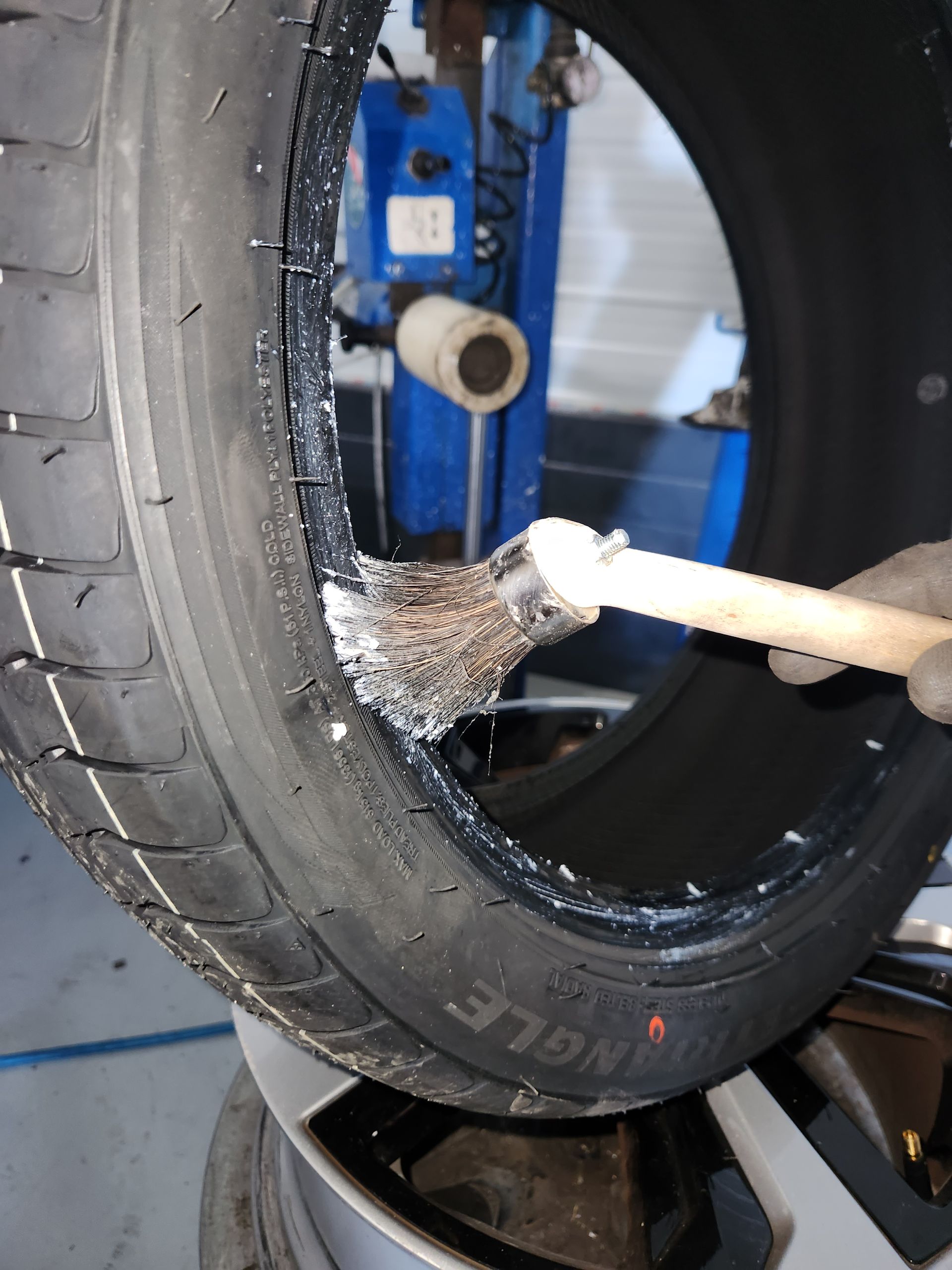 Dans un garage, un mécanicien portant des gants de travail tient un ensemble pneu-roue à la verticale.