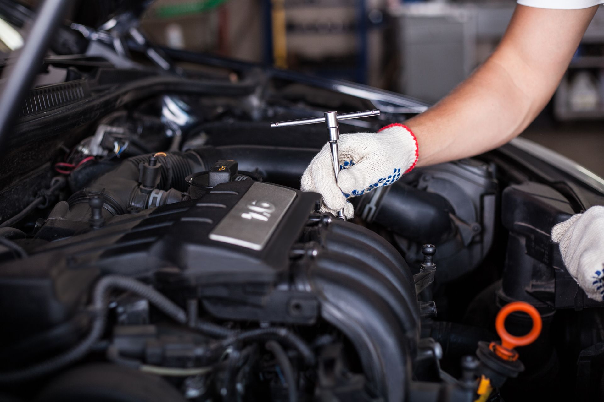 Dans un atelier de réparation, un mécanicien portant des gants de travail blancs utilise un outil pour serrer un boulon sur le moteur d'une voiture.