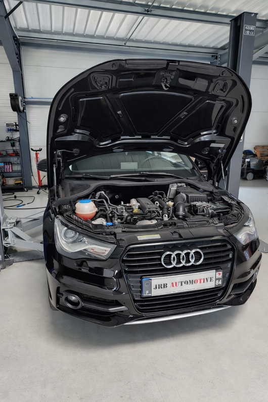 Audi noire, capot ouvert, dans un garage, laissant apparaître le compartiment moteur et la calandre.