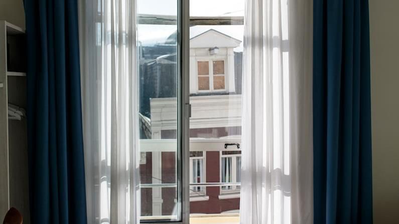 View through sheer curtains of a building across the street, with blue drapes framing the window.