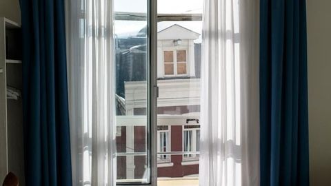 View through sheer curtains of a building across the street, with blue drapes framing the window.