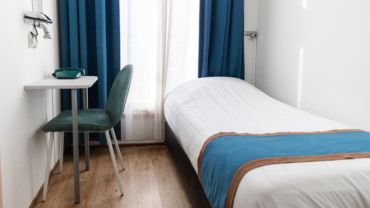 Small bedroom with a single bed, desk, chair, and blue curtains by a window.