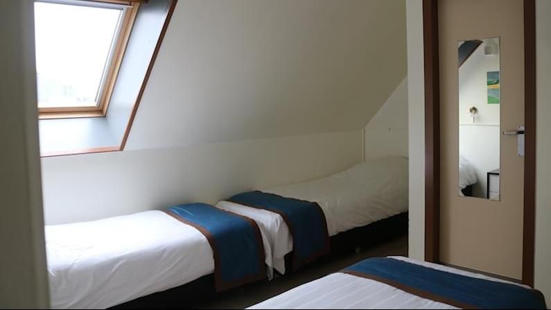 Small attic bedroom with three white beds, blue throws, and a skylight window