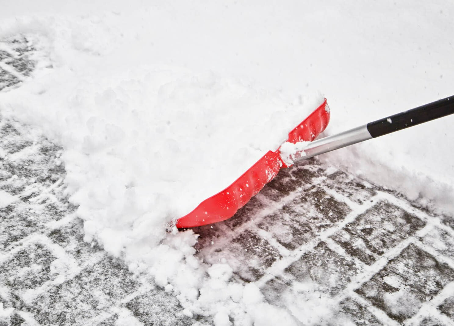 Premier plan du déneigement de trottoir avec une pelle rouge