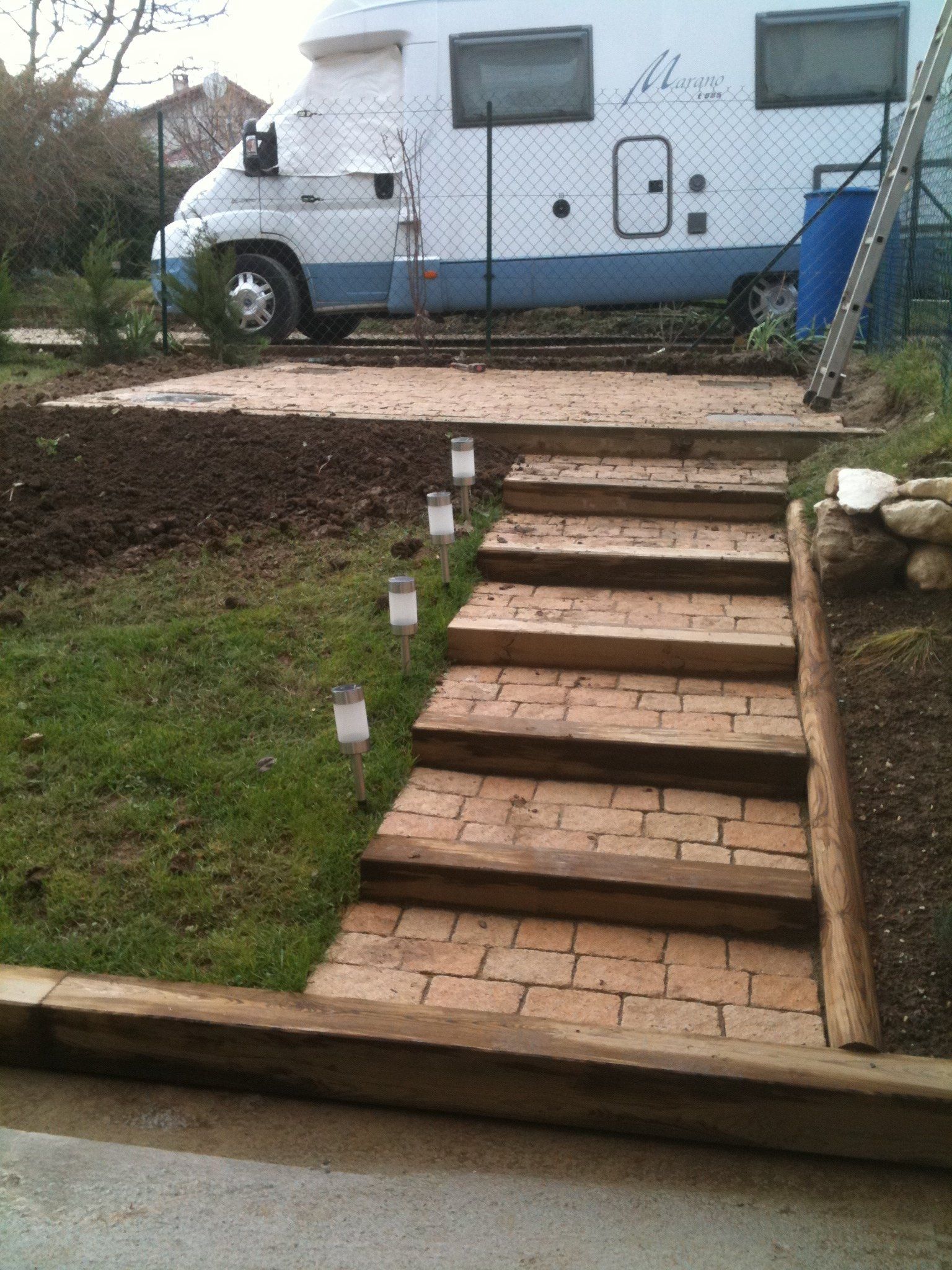 Petits escaliers extérieurs en pierre beige et en bois avec un fourgon au fond