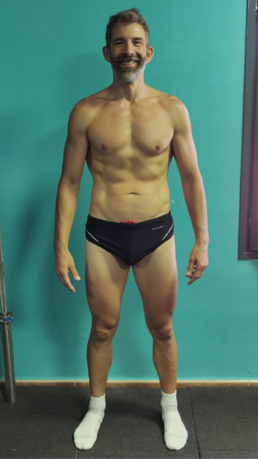 Un hombre sin camisa y en ropa interior está parado frente a una pared azul.