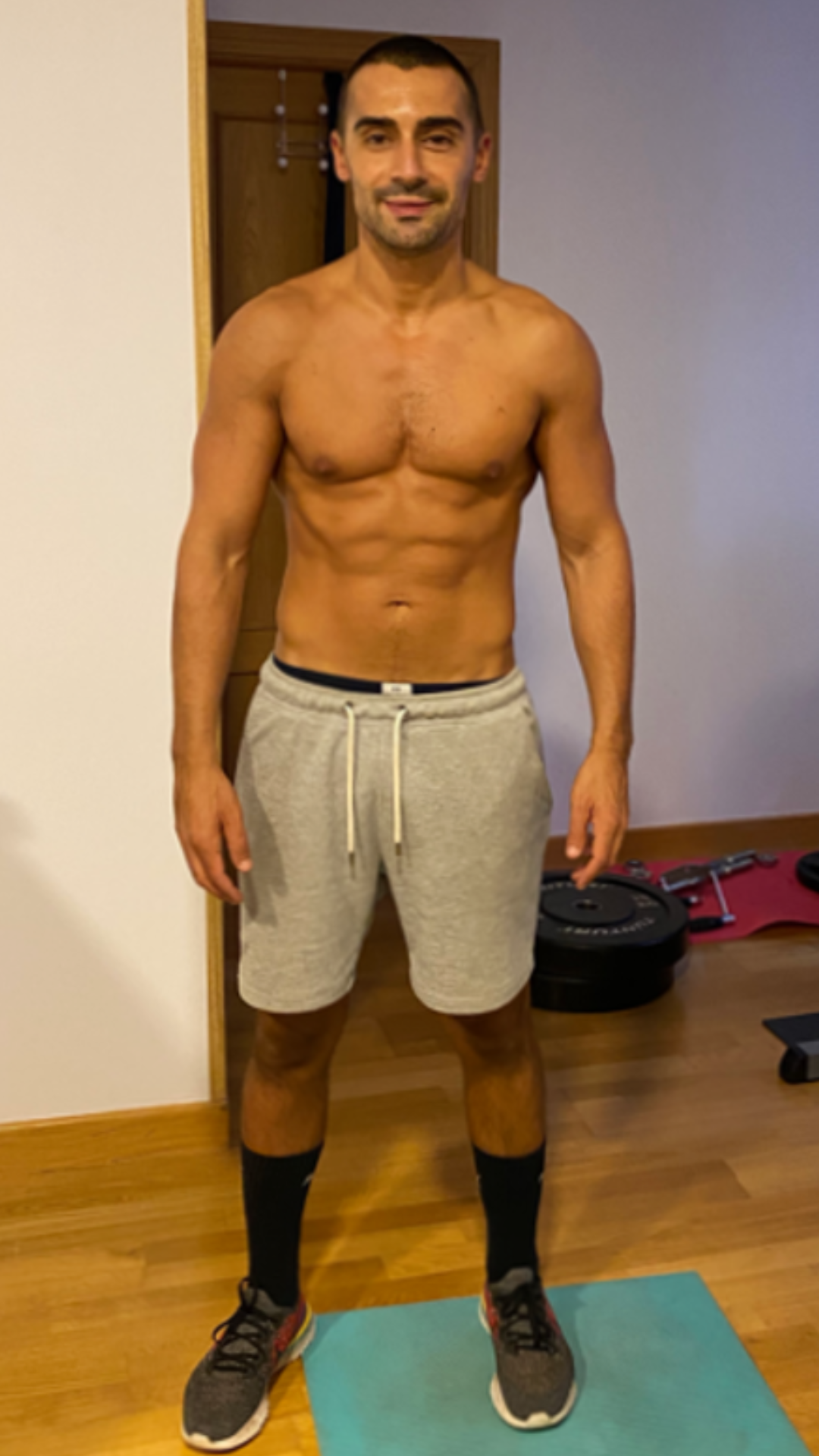 Un hombre sin camisa está de pie sobre una colchoneta de yoga en una habitación.