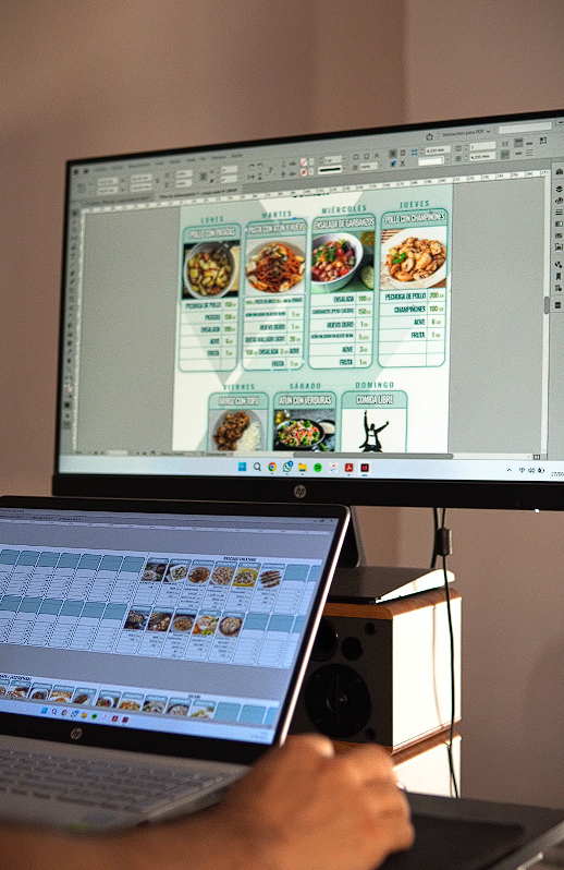 Una persona está usando una computadora portátil y una computadora para crear un menú para un restaurante.
