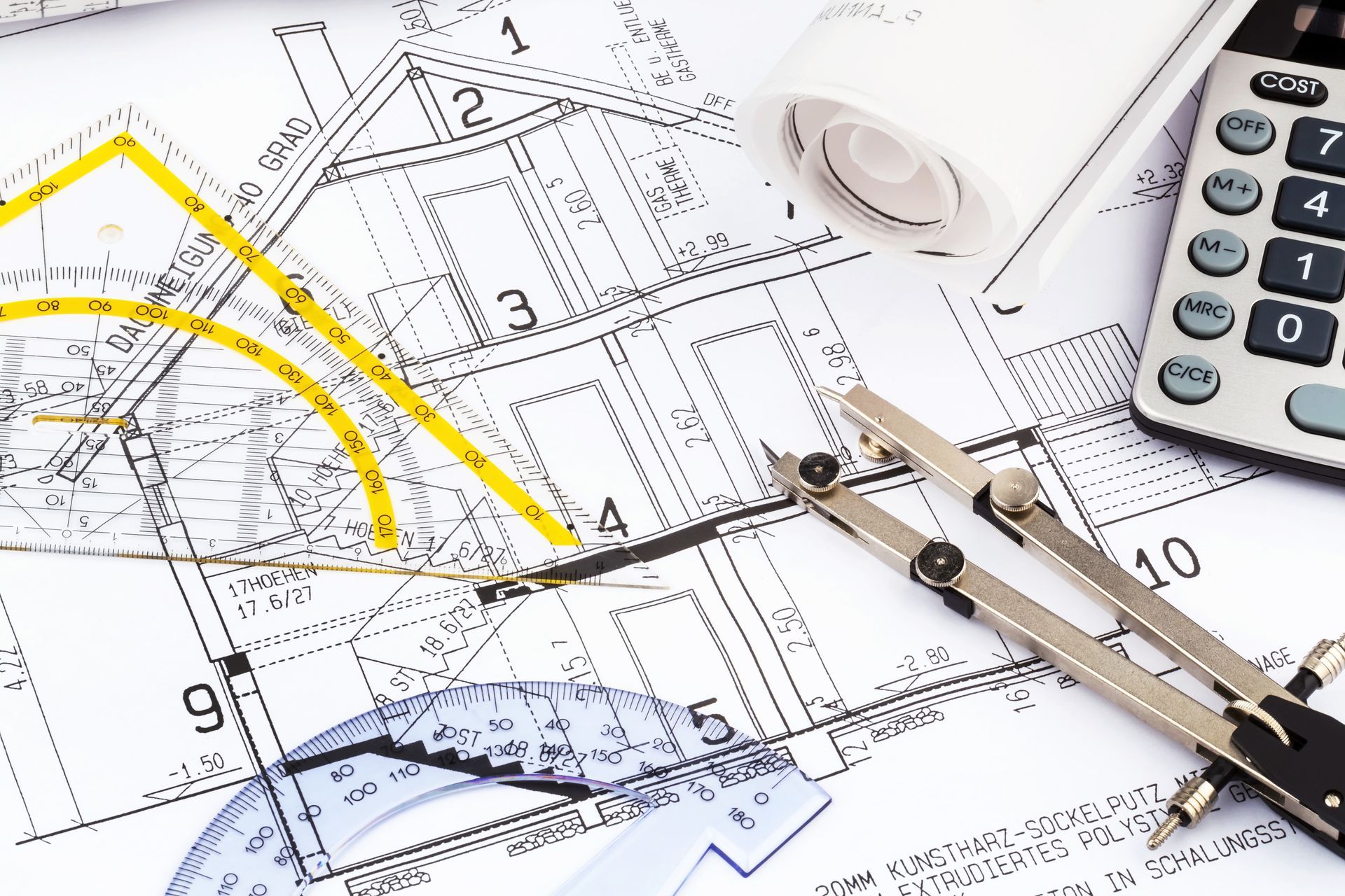 Plans architecturaux avec des outils comme une calculatrice, un compas et des plans enroulés.