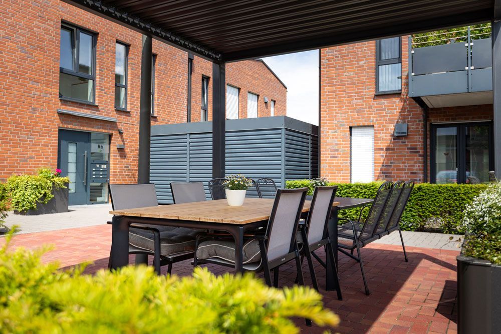 Überdachte Terrasse mit Esstisch und Stühlen in einem Backstein-Innenhof eines Mehrfamilienhauses