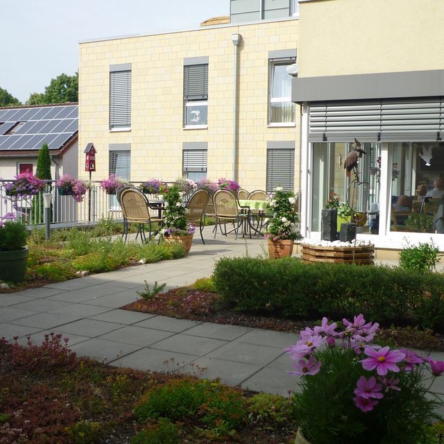 Innenhof mit Tischen, Stühlen, Blumen und einem modernen Gebäude mit Solarpaneelen