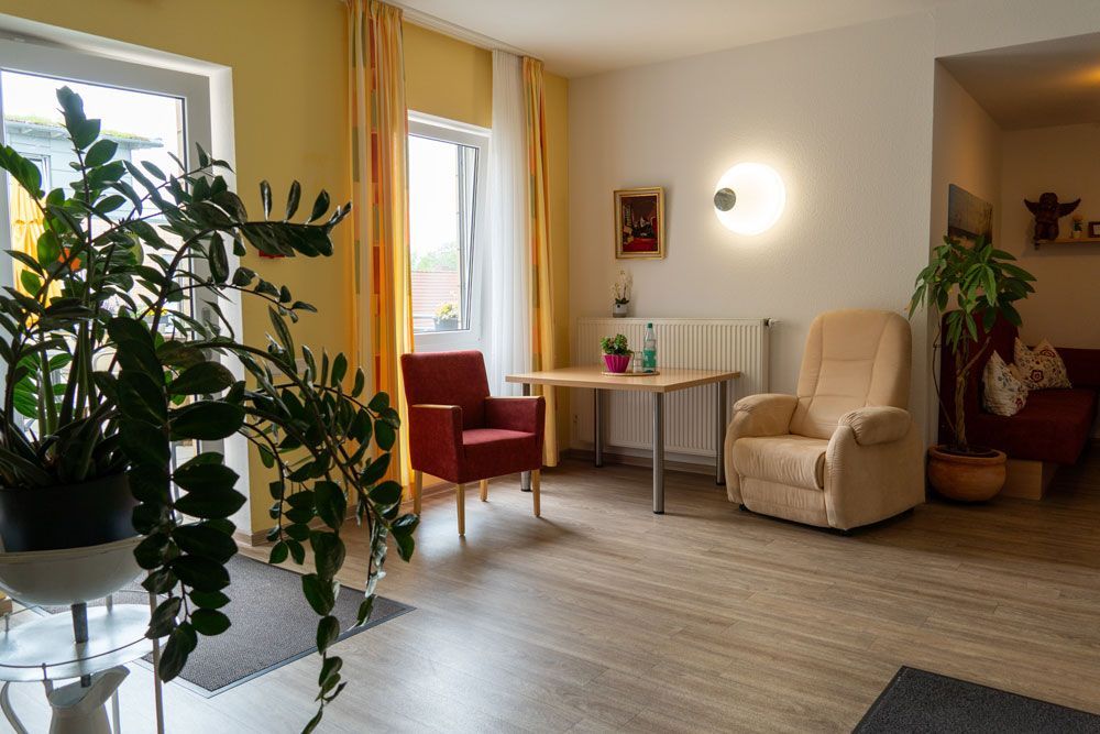 Helles Wohnzimmer mit Topfpflanzen, zwei Stühlen, einem kleinen Tisch und großen Fenstern
