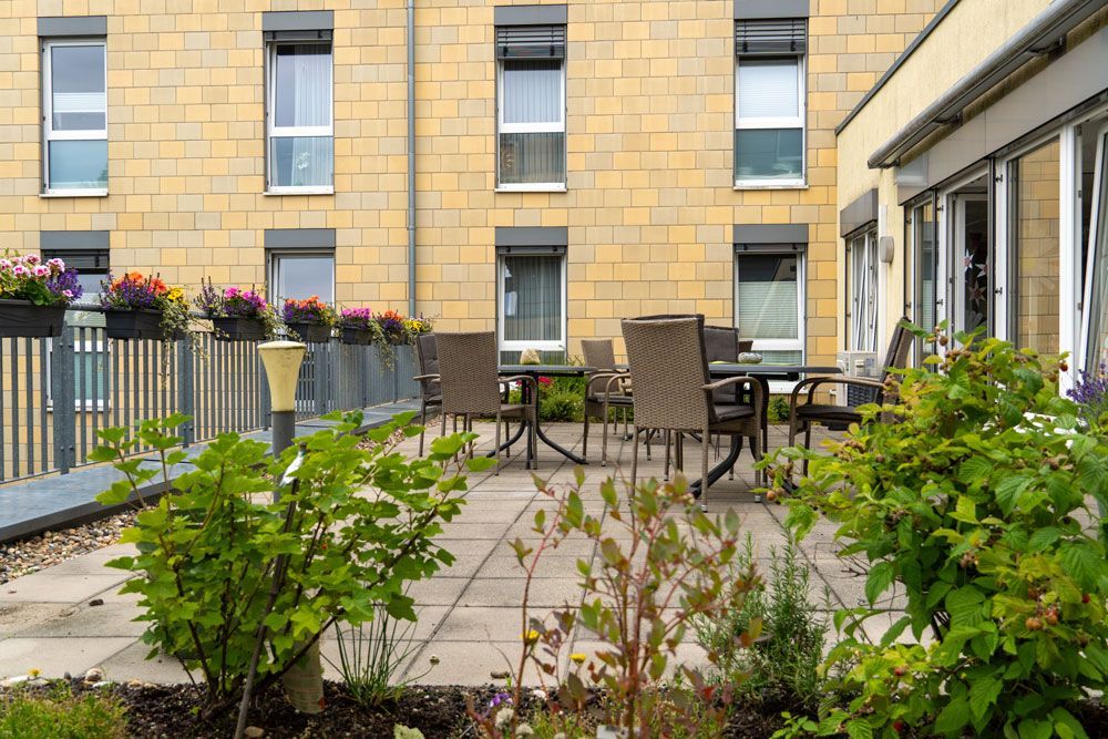 Innenhofterrasse mit Tischen, Stühlen, Blumenkästen und Grünpflanzen neben einem Backstein-Wohnhaus