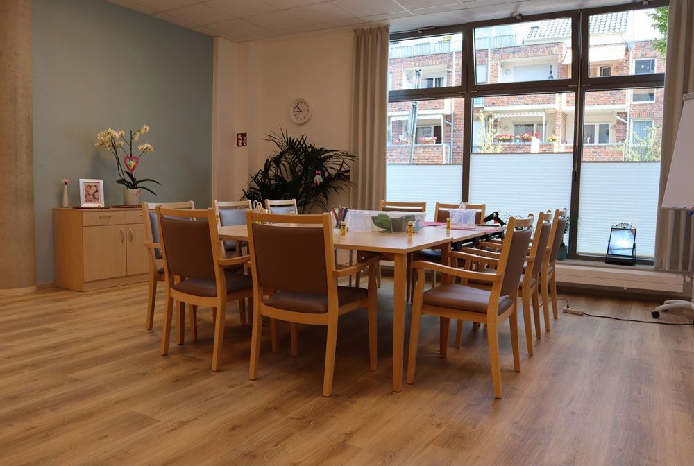Helles Esszimmer mit langem Holztisch, Stühlen, Pflanzen und großen Fenstern mit Blick auf einen Innenhof
