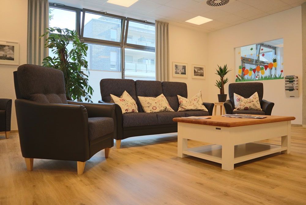 Modernes Wohnzimmer mit dunklem Sofa, Sessel, Couchtisch, großen Fenstern und Holzboden.