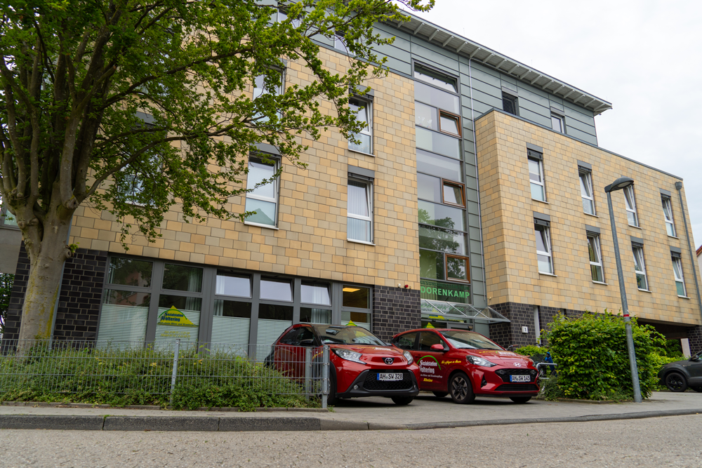Modernes Mehrfamilienhaus mit Backsteinfassade, großen Fenstern und zwei roten Autos, die davor parken