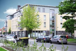 Modernes Mehrfamilienhaus an einer Stadtstraße mit parkenden Autos und Bäumen