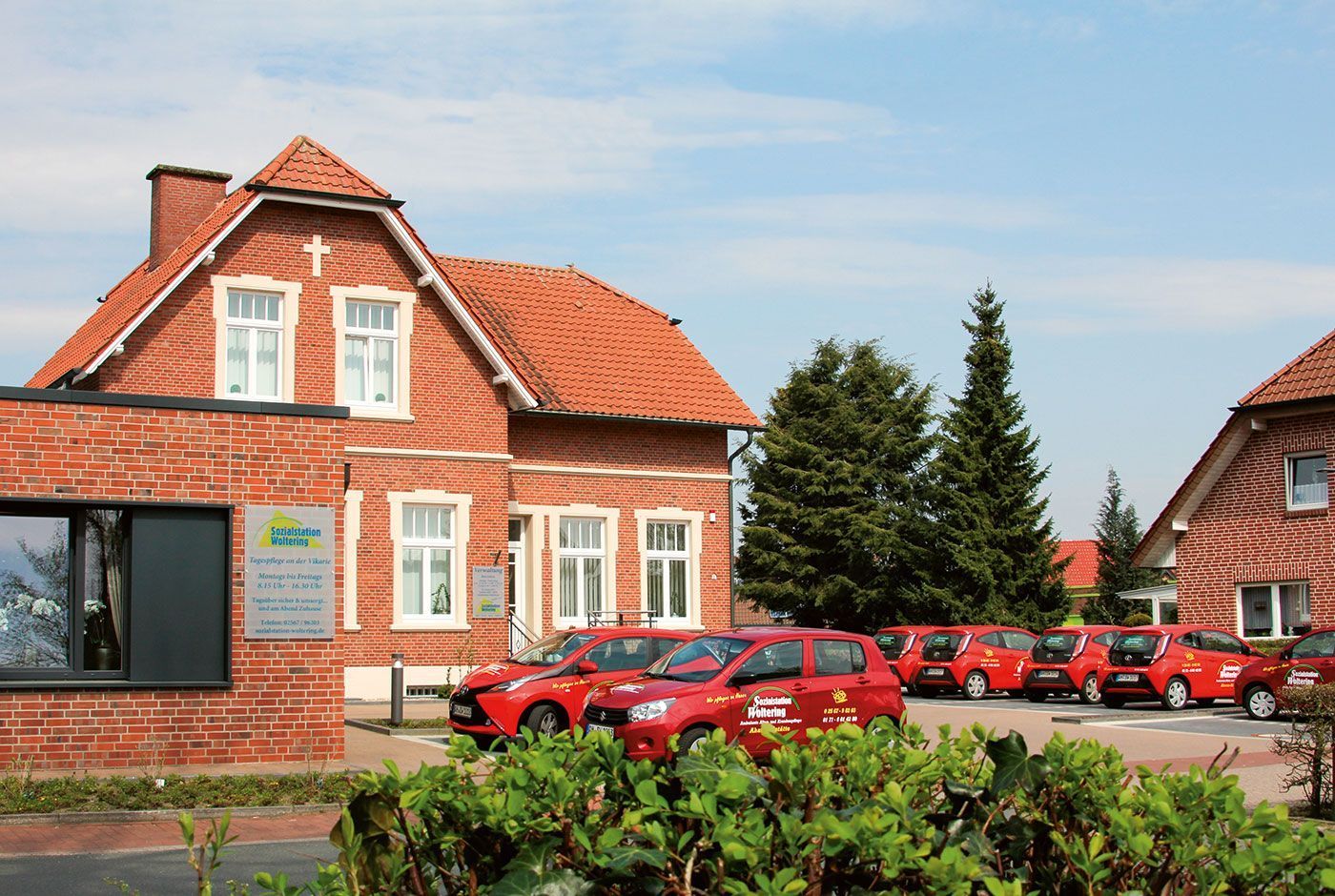 Ein Backsteingebäude mit rotem Ziegeldach und mehrere rote Autos, die davor unter blauem Himmel parken
