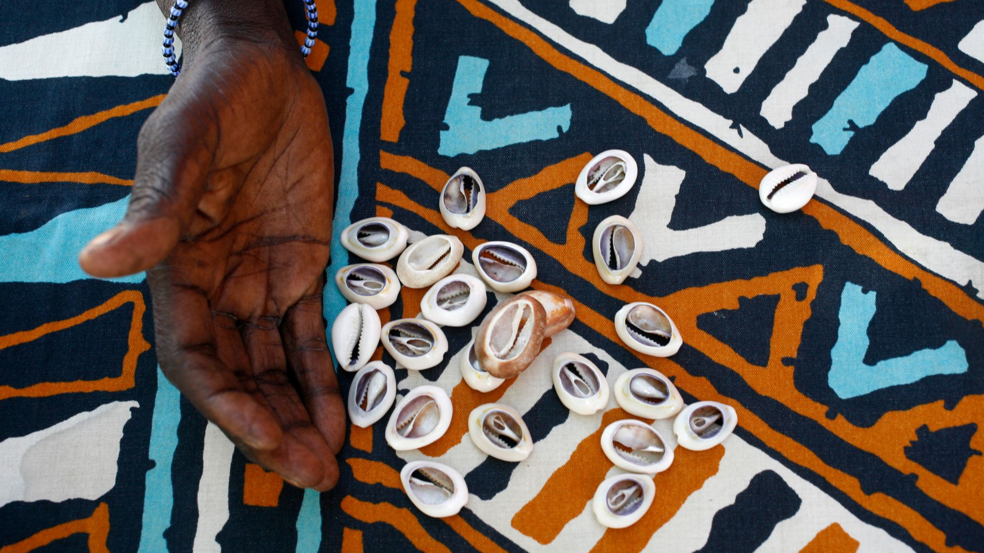 Main à côté de coquillages cauris sur un tissu à motifs.