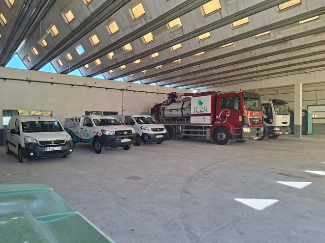 Un camion-benne blanc charge des feuilles dans une rue résidentielle, le long d'un trottoir, sous un ciel bleu dégagé.
