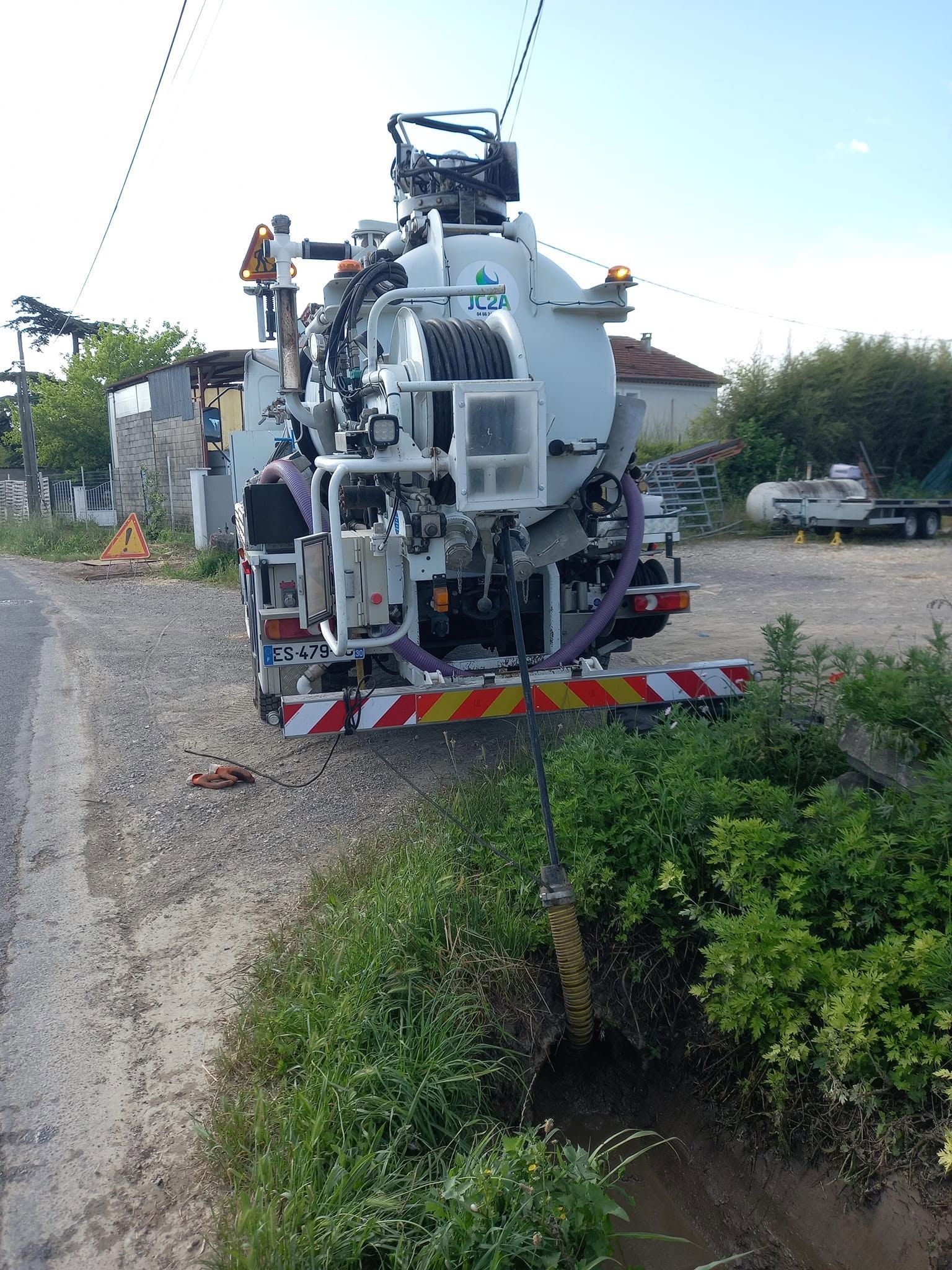 Camion utilitaire sur une route de campagne, travaillant au bord d'un fossé, tuyaux et équipements déployés au-delà du talus.