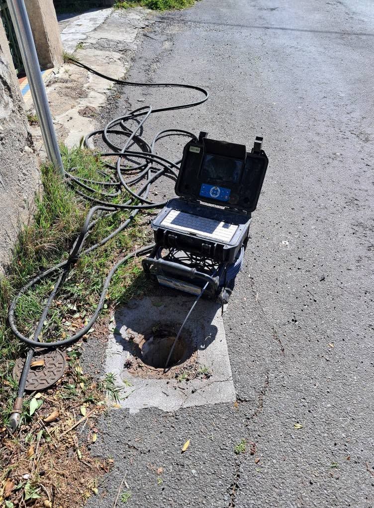 Caméra d'inspection des services publics en bordure de trottoir au-dessus d'un regard d'égout ouvert sur une route asphaltée fissurée