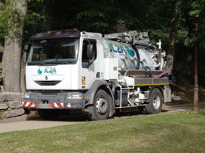 Camionnette utilitaire blanche stationnée sur l'herbe à côté d'arbres, avec du matériel monté à l'arrière.