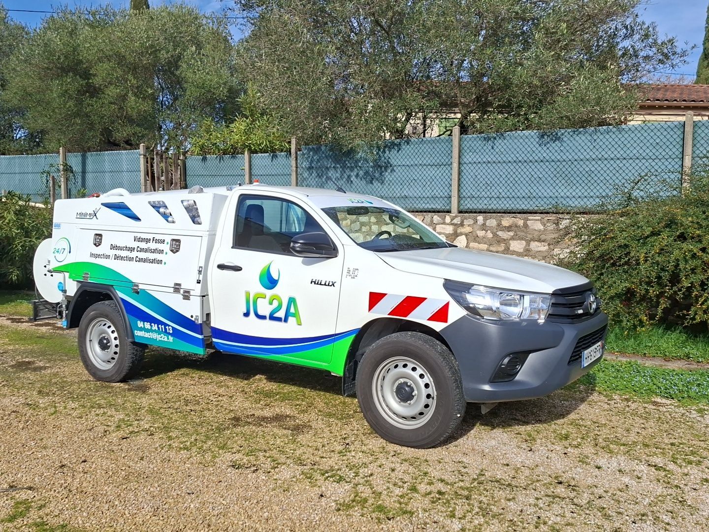 Camionnette utilitaire blanche avec logo vert garée à côté d'un immeuble et de buissons.