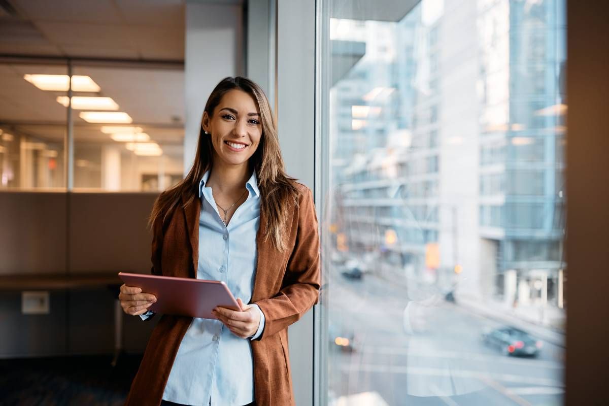 A woman is standing in front of a window holding a tablet.