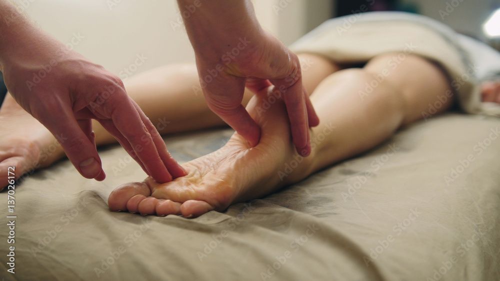 Hände massieren Fuss und Knöchel einer Person, die auf einer Massageliege liegt.