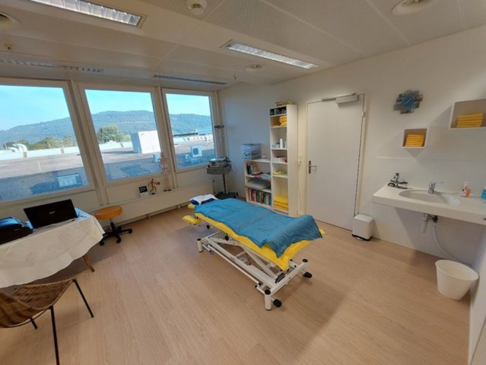 Untersuchungsraum mit Massageliege, Waschbecken, Fenster und Zubehör.