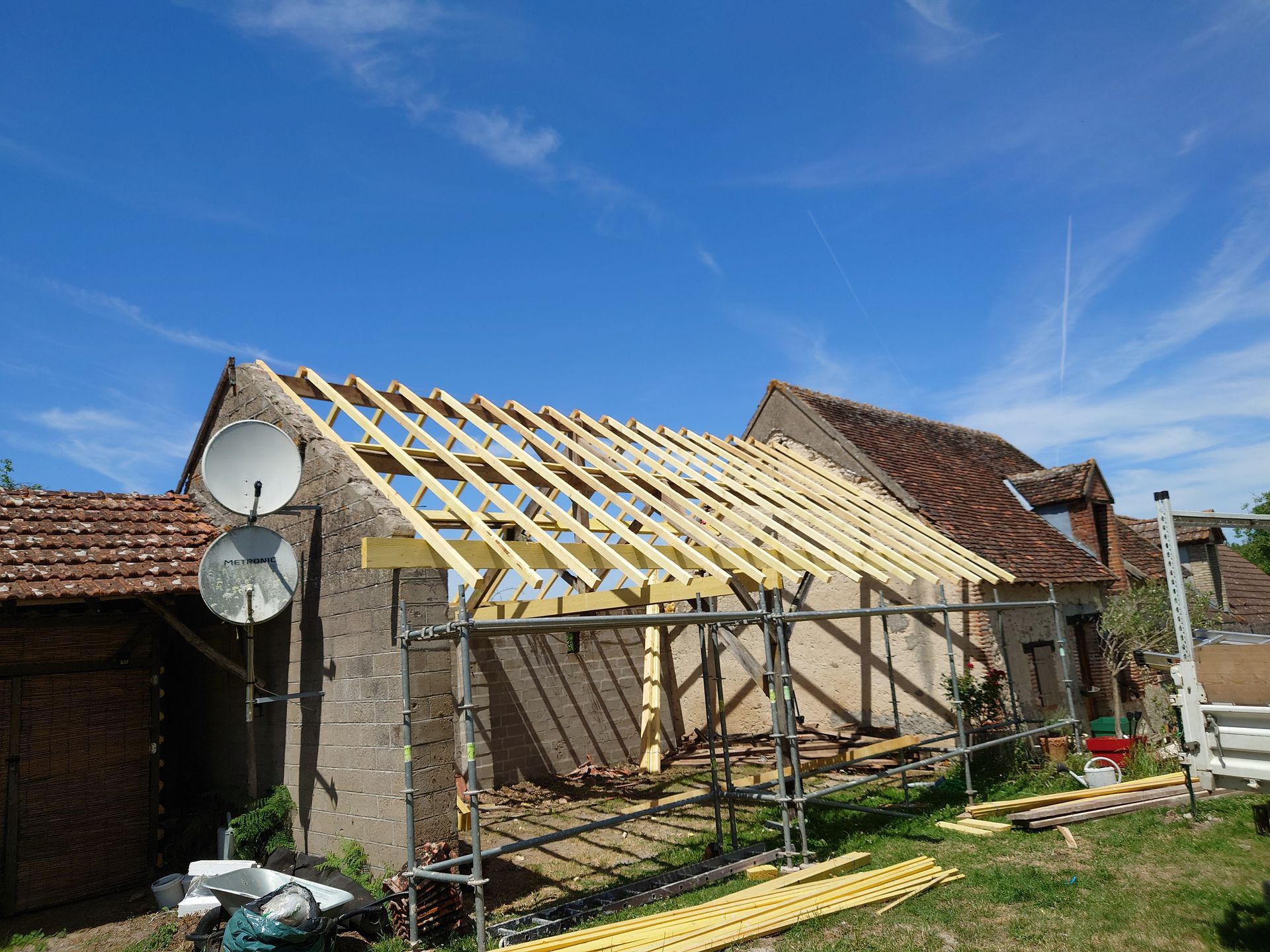 Chantier de construction montrant un bâtiment avec une nouvelle charpente de toit en bois, entouré d'échafaudages.