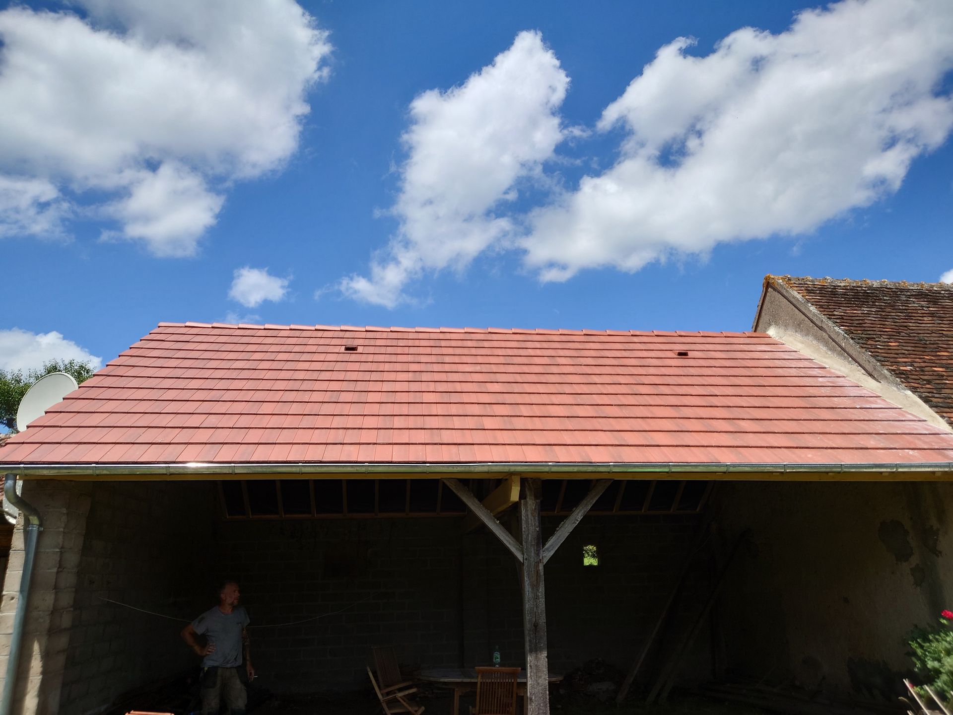 Une personne se tient sous un toit de tuiles rouges fraîchement posé, sur une structure ouverte.