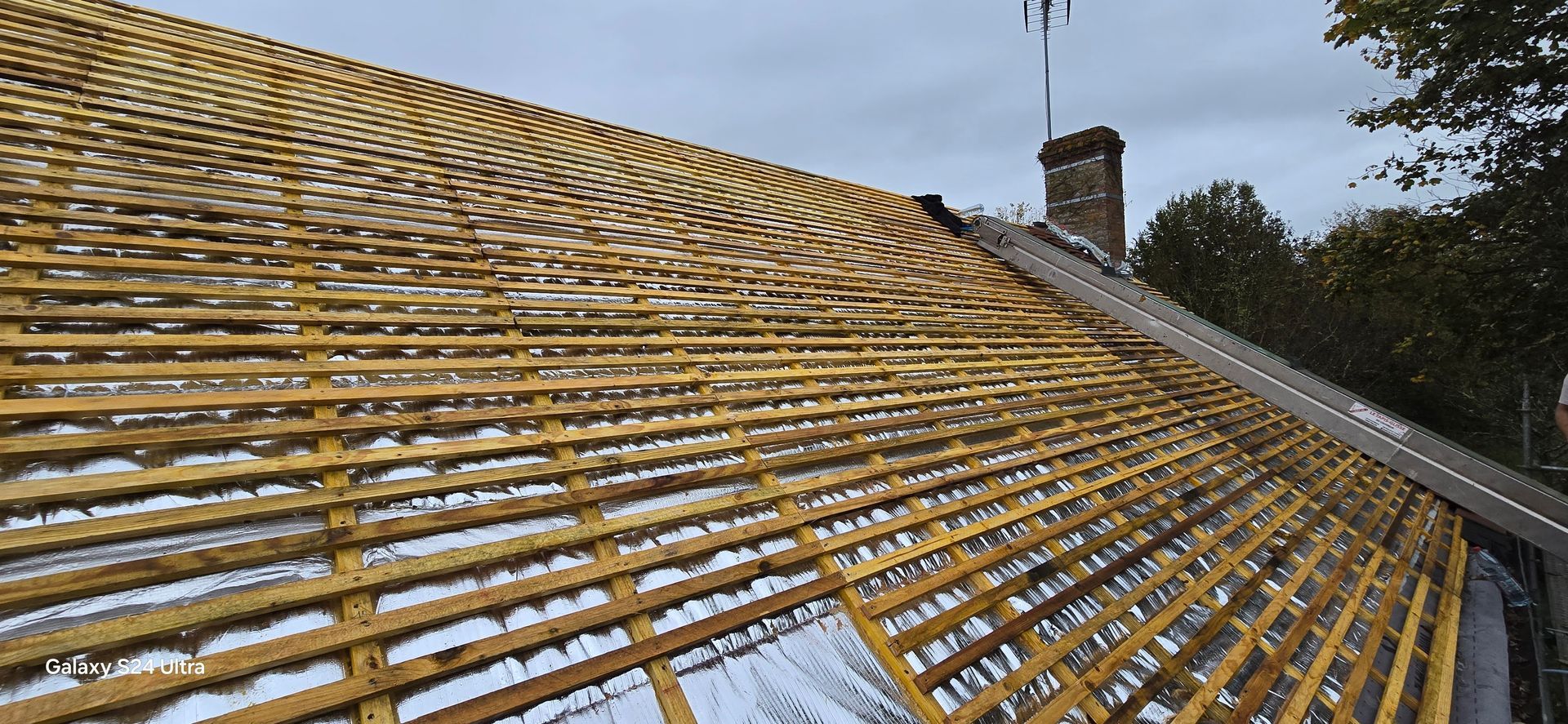Une toiture en rénovation, présentant un motif incurvé de liteaux en bois installés sur une membrane protectrice blanche.