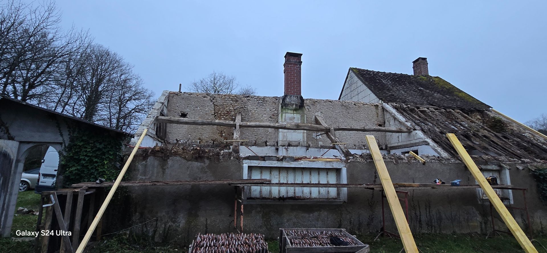 Une maison en rénovation, dont le toit a été enlevé, laissant apparaître la charpente intérieure et la maçonnerie.
