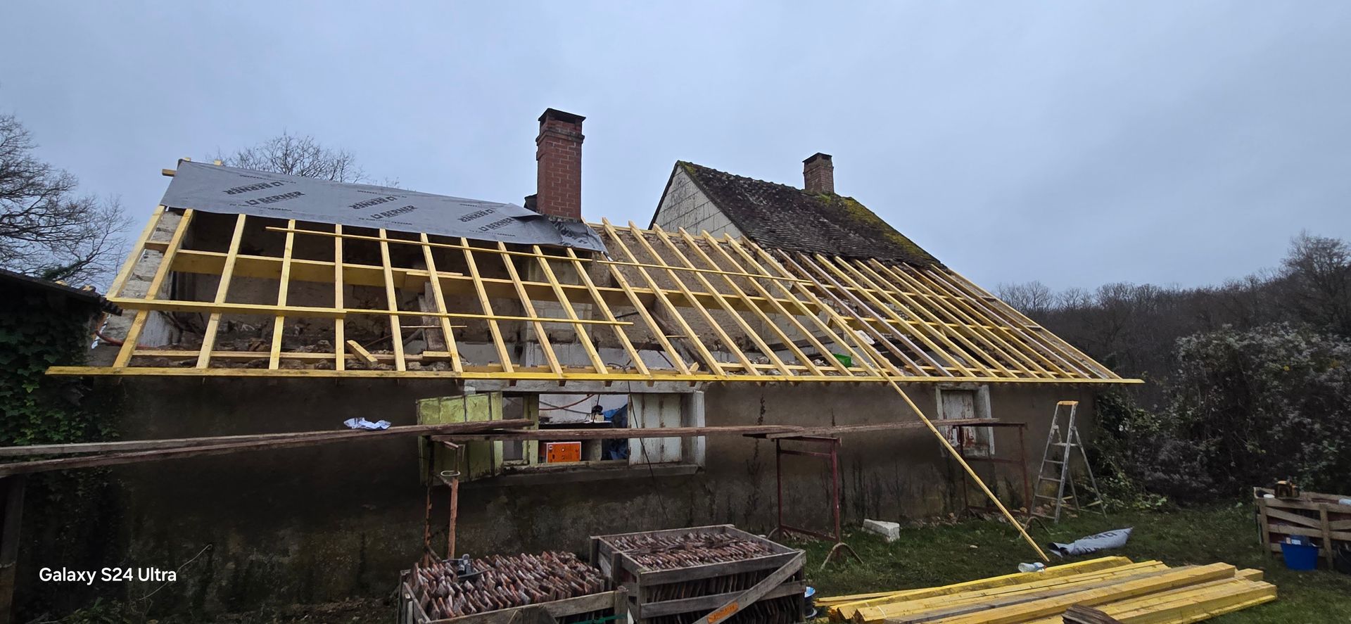 Un toit en cours de rénovation avec de nouveaux chevrons en bois apparents et une sous-couche de toiture partielle installée.