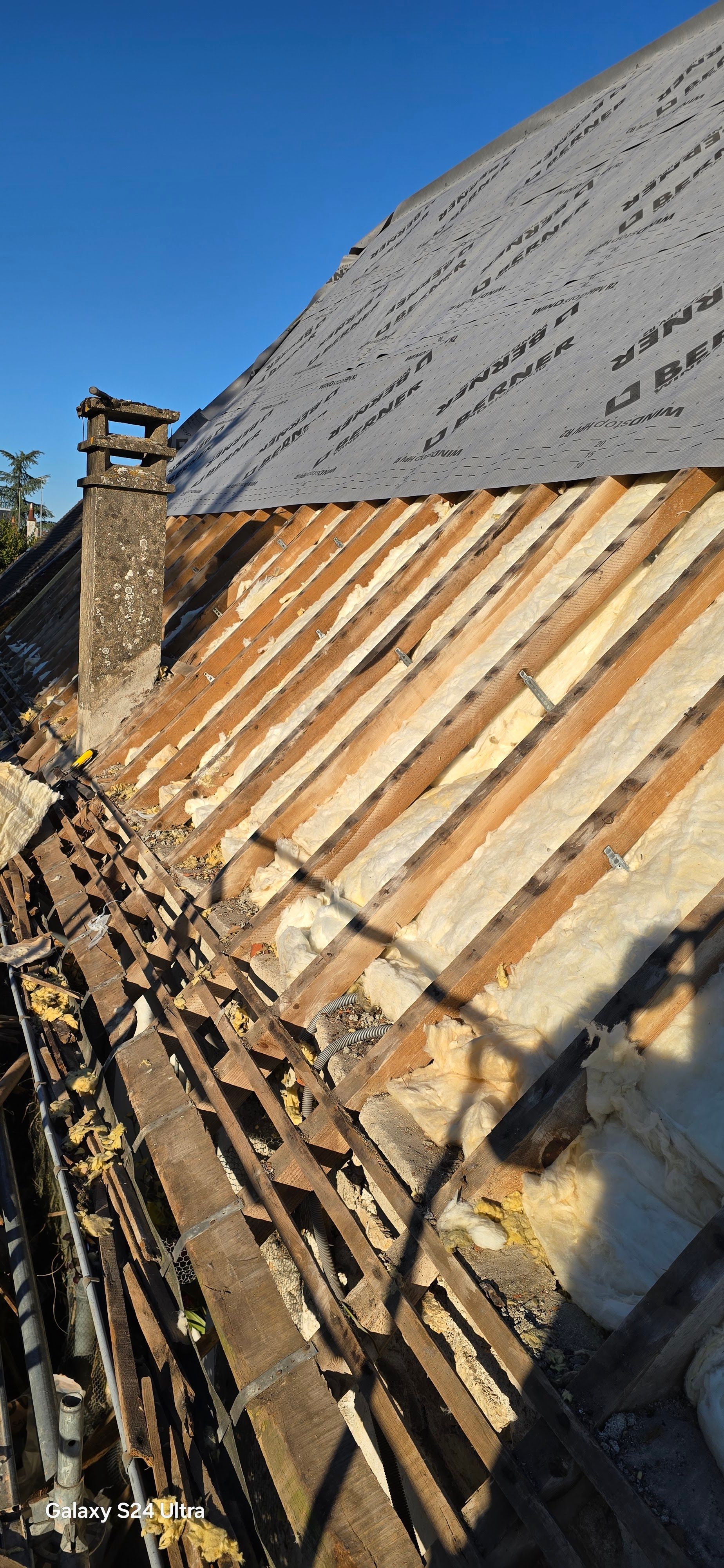 Toiture en cours de rénovation : pose d'ardoises sur chevrons en bois, laissant apparaître l'isolation.