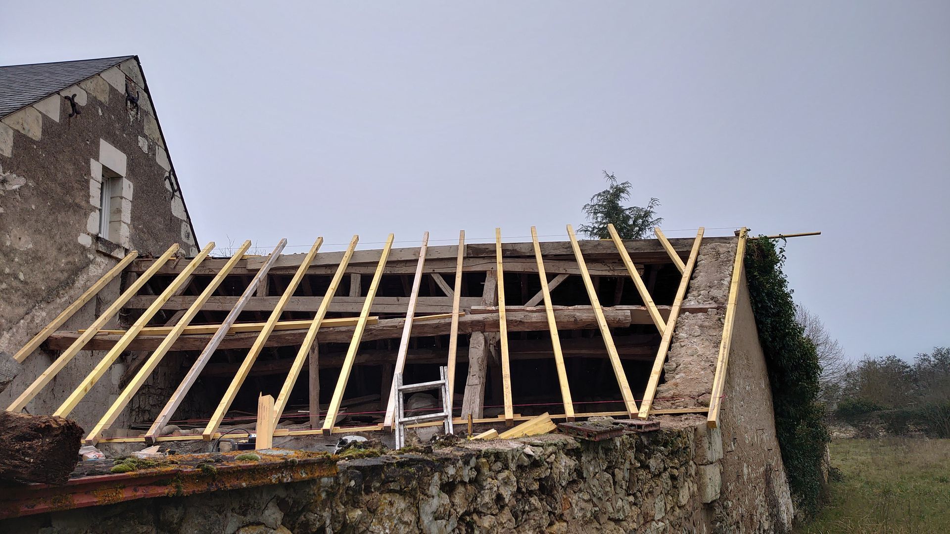 Toiture en rénovation sur une maison en pierre, avec charpente apparente.